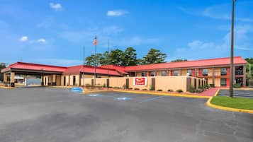A hotel with a red roof, a parking lot, and a flag.