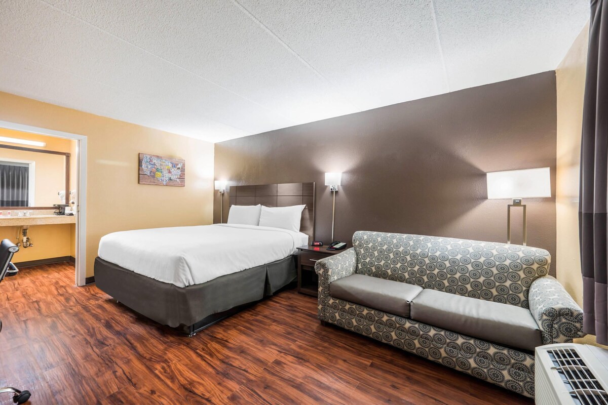 Een hotelkamer met een bed, een bank, een bureau met een computer en een wandlamp.