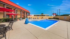 Un hotel con piscina, mobiliario exterior y un edificio de techo rojo.