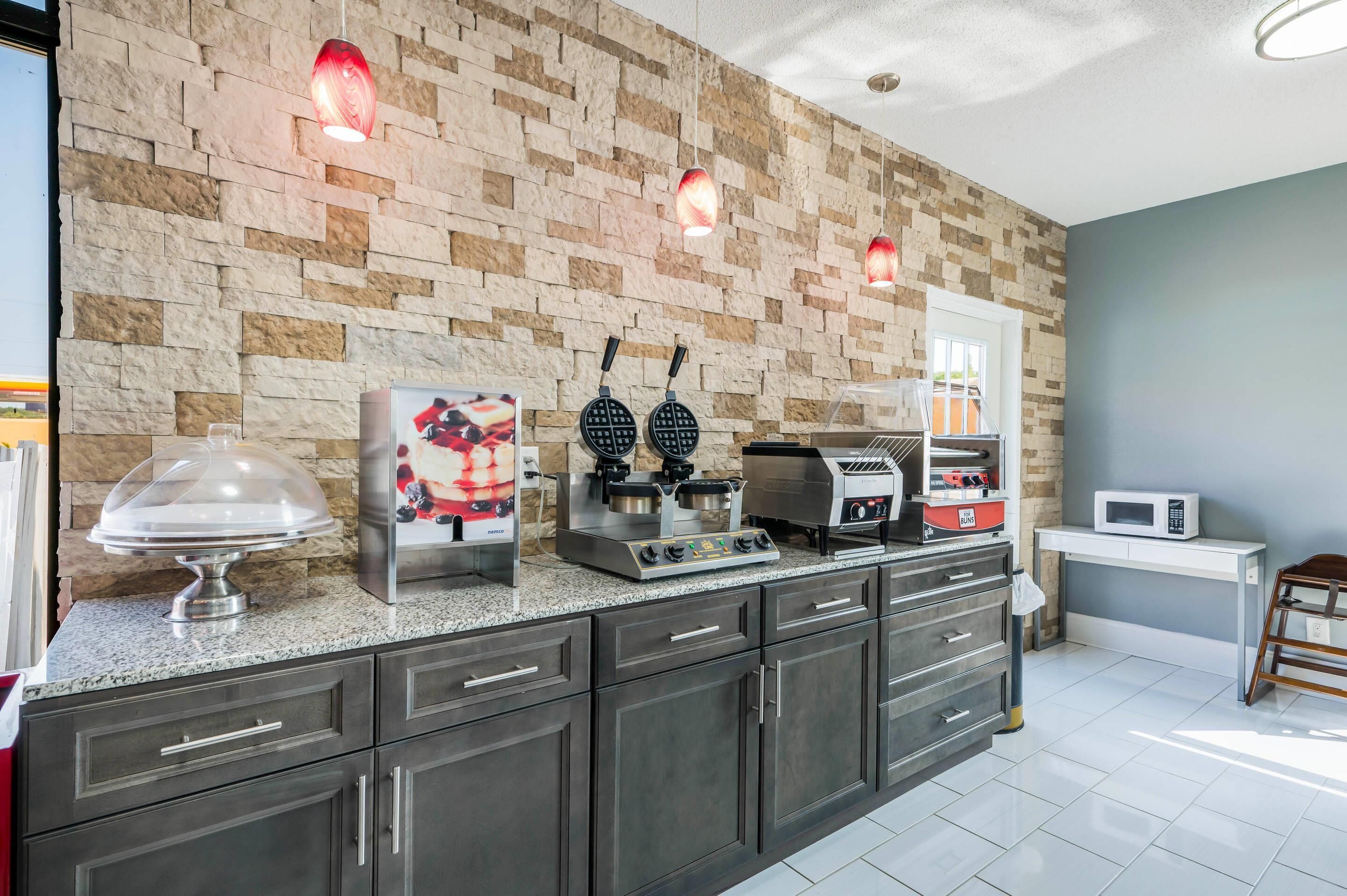 A kitchen with a stone wall, a waffle maker, a coffee machine, and a microwave.