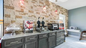 A kitchen with a stone wall, a waffle maker, a coffee machine, and a microwave.