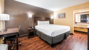 Habitación de hotel con cama, escritorio, silla, lámpara y un cuadro en la pared.