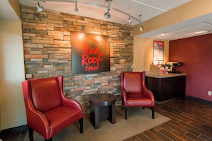 A Red Roof Inn lobby with a stone wall, two leather chairs, a small table, and a reception desk with amenities. - Red Roof Inn Rockford East – Casino District (Rockford)
