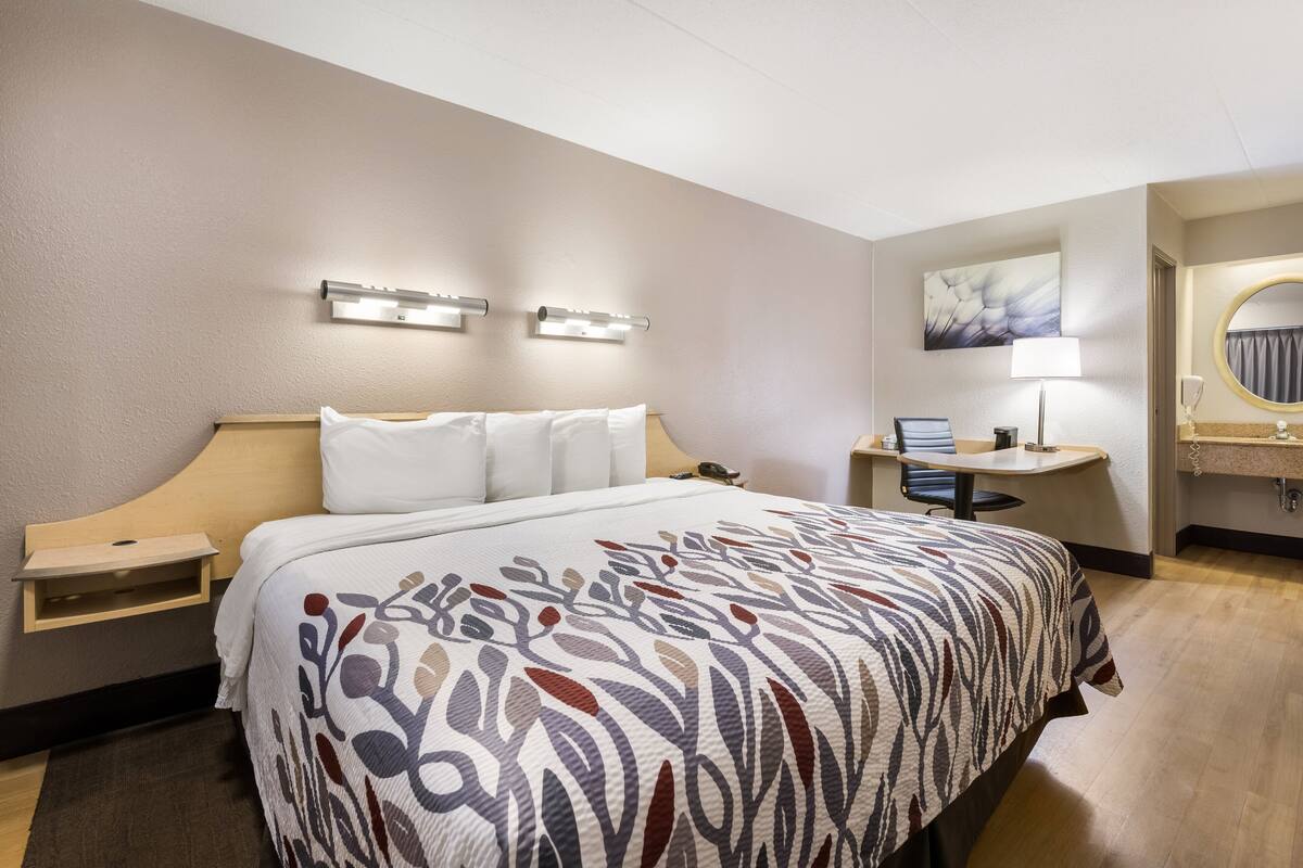 Ein Hotelzimmer mit Bett, Nachttischen, Schreibtisch, Stuhl, Lampe und Spiegel.