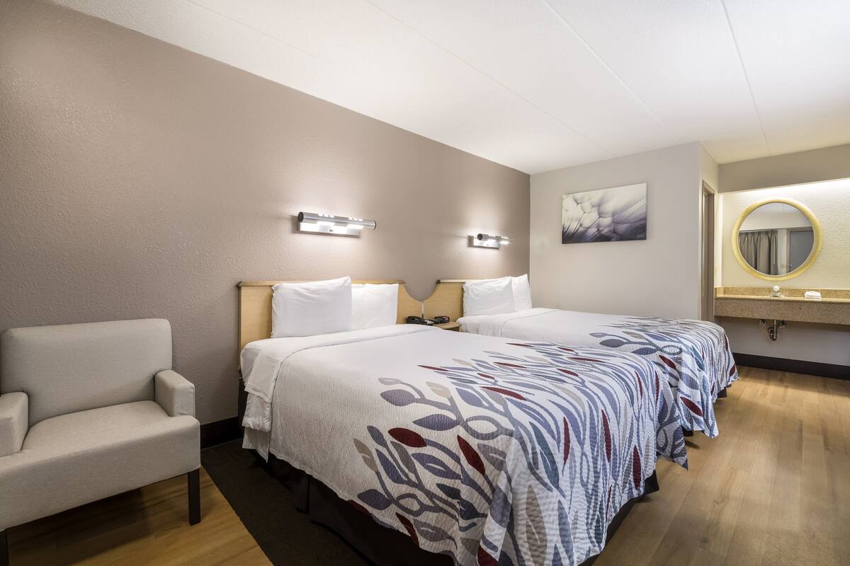 Ein Hotelzimmer mit zwei Betten, einem Sessel, einem Nachttisch, einem Spiegel und einem Bild an der Wand.
