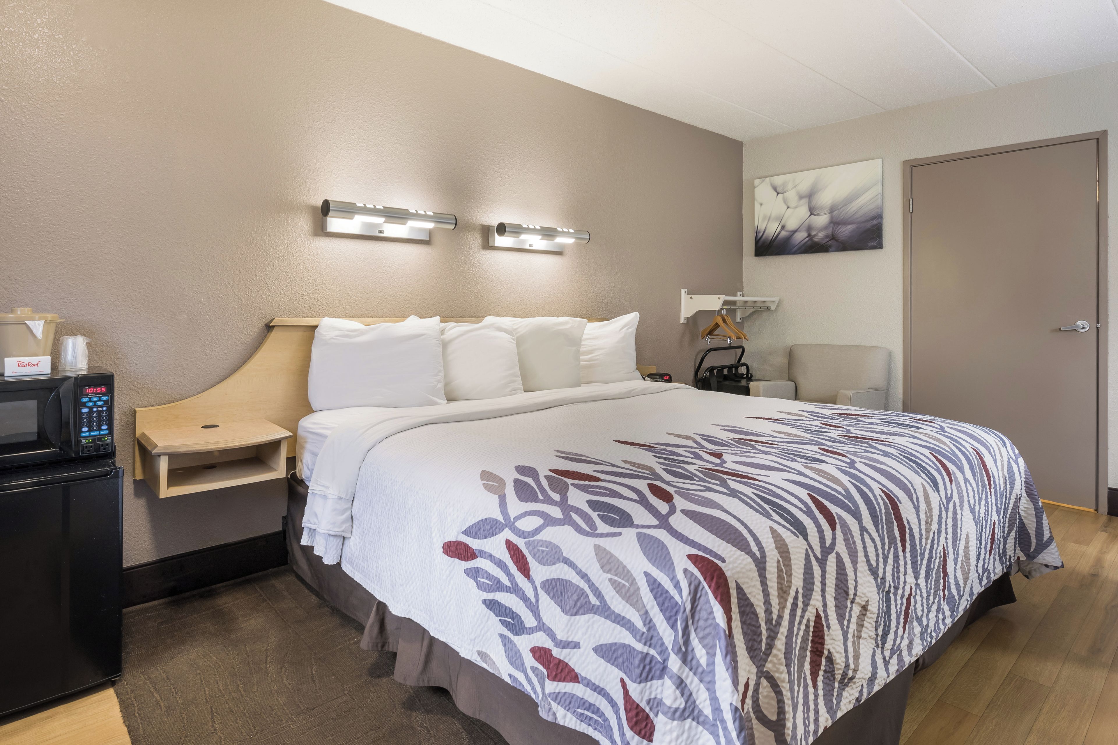 Una habitación de hotel con cama, mesita de noche, microondas y un reloj.