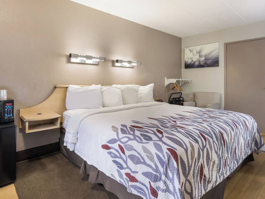 Una habitación de hotel con cama, mesita de noche, microondas y un reloj.