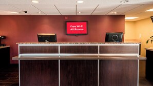 A reception desk with a flat-screen TV displaying 'Free Wi-Fi All Rooms' in a hotel lobby. - Red Roof Inn Rockford East – Casino District (Rockford)
