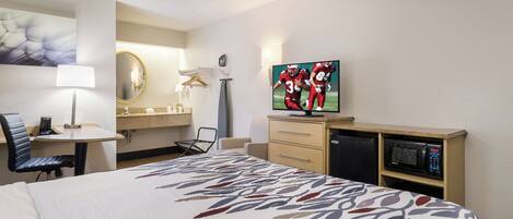 A hotel room with a bed, a desk with a chair, a television, a mirror, and a microwave.