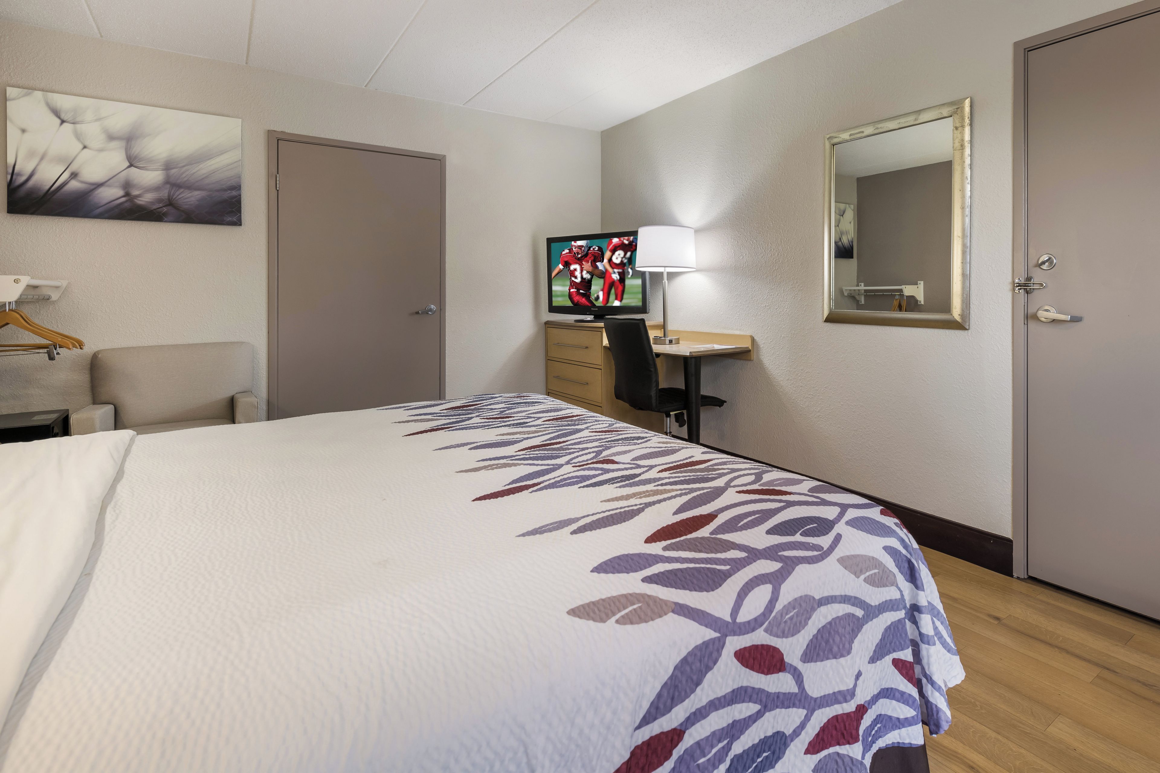 A hotel room with a bed, a desk with a computer, a TV, a chair, and a mirror.