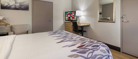 A hotel room with a bed, a desk with a computer, a TV, a chair, and a mirror.