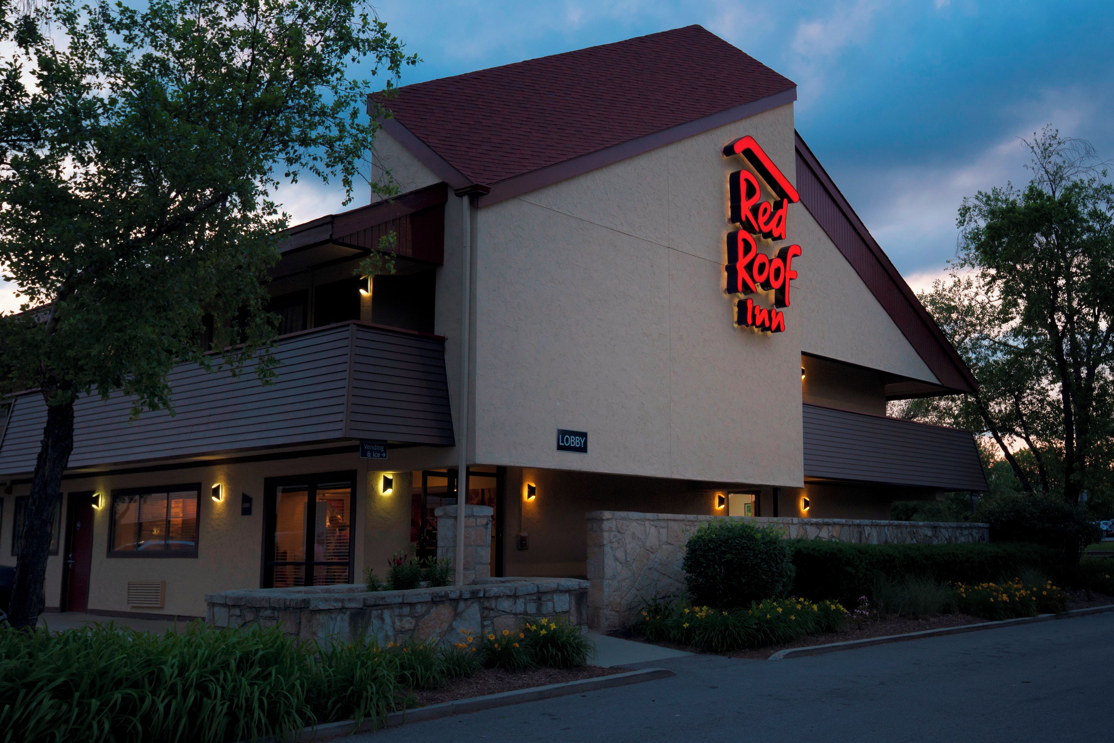 A Red Roof Inn with a prominent neon sign, a stone facade, and a balcony.