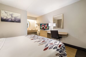Une chambre d’hôtel comprenant un lit, un bureau avec un ordinateur, une télévision, un miroir et une salle de bain.