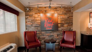 A Red Roof Inn lobby with two leather chairs, a small table, and a stone wall. - Red Roof Inn Rockford East – Casino District (Rockford)