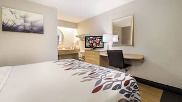 A hotel room with a bed, a desk, a television, a mirror, and a wall art piece.