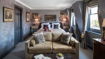 A hotel room with a large bed, two bedside tables with lamps, a sofa, and a window with curtains.