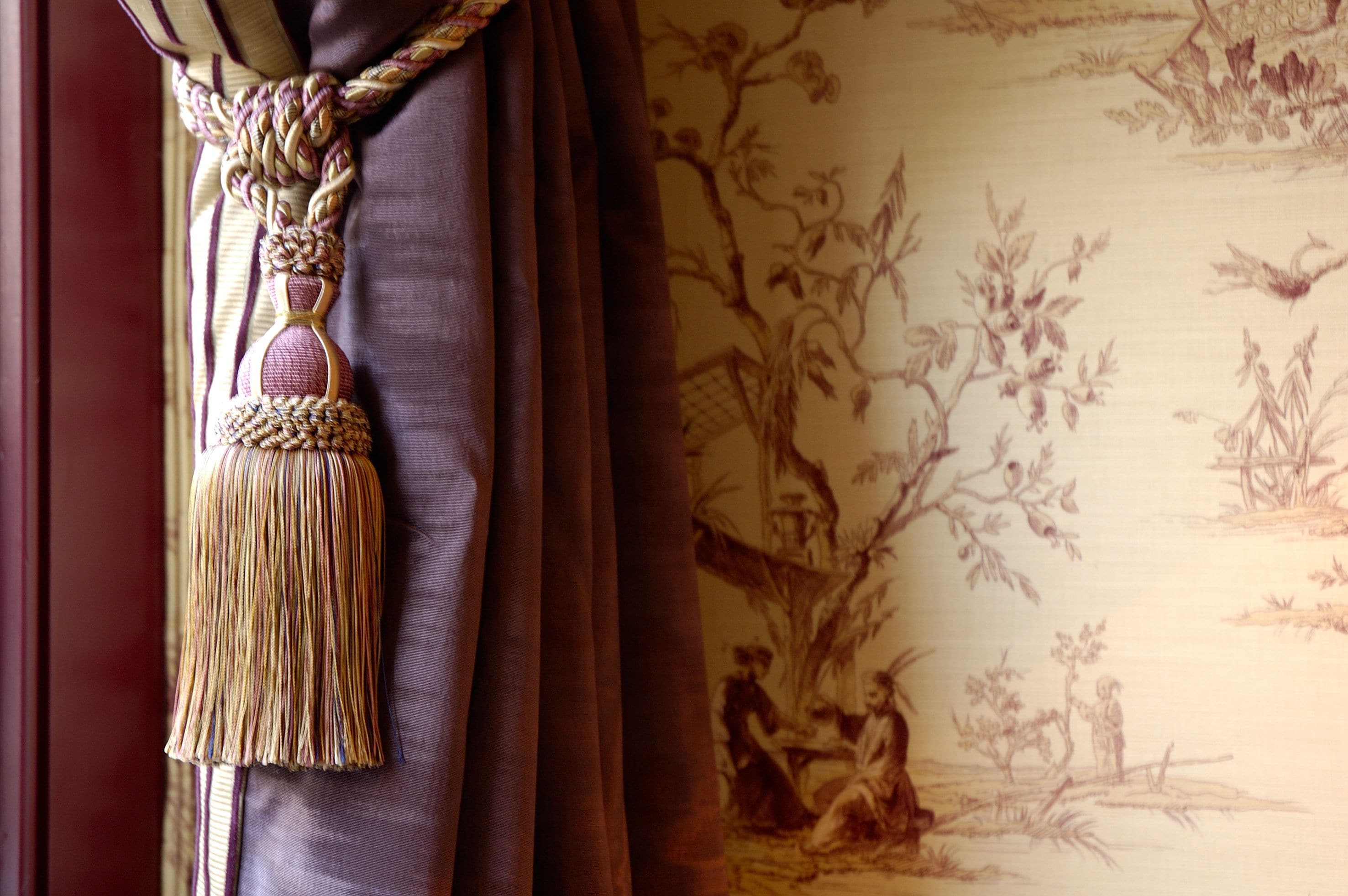 A curtain with a tassel and a floral wallpaper pattern.