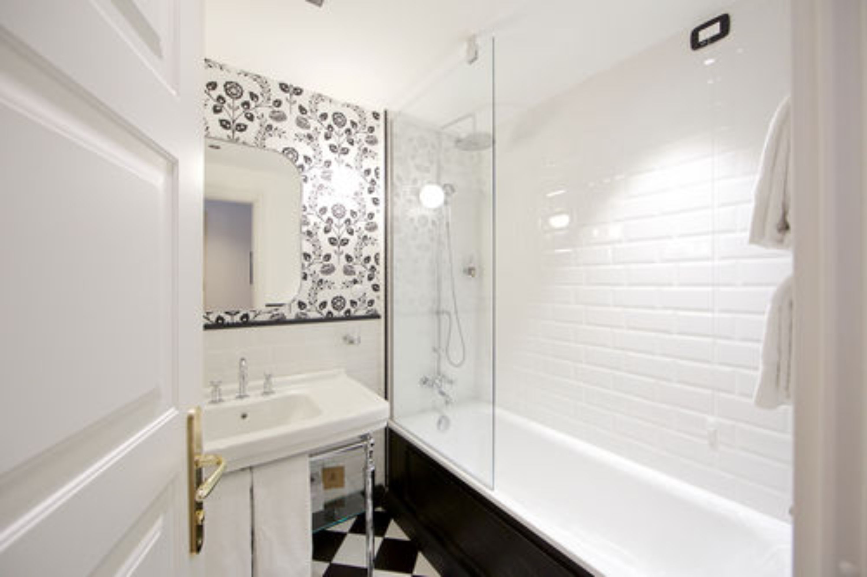 Un baño con lavamanos blanco, ducha envuelta en vidrio y espejo con diseño.