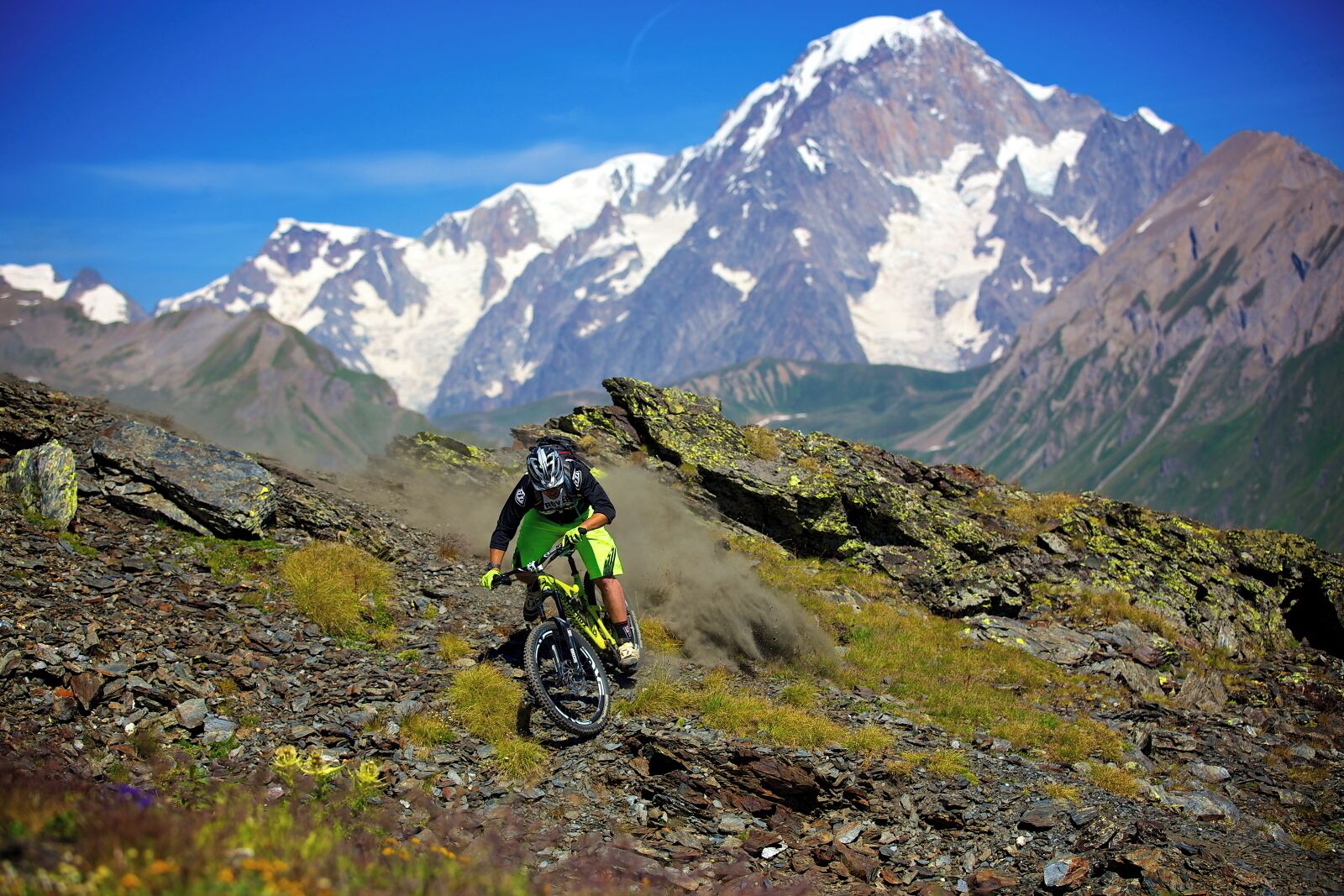 A mountain biker on a rocky trail with a mountain range in the background.