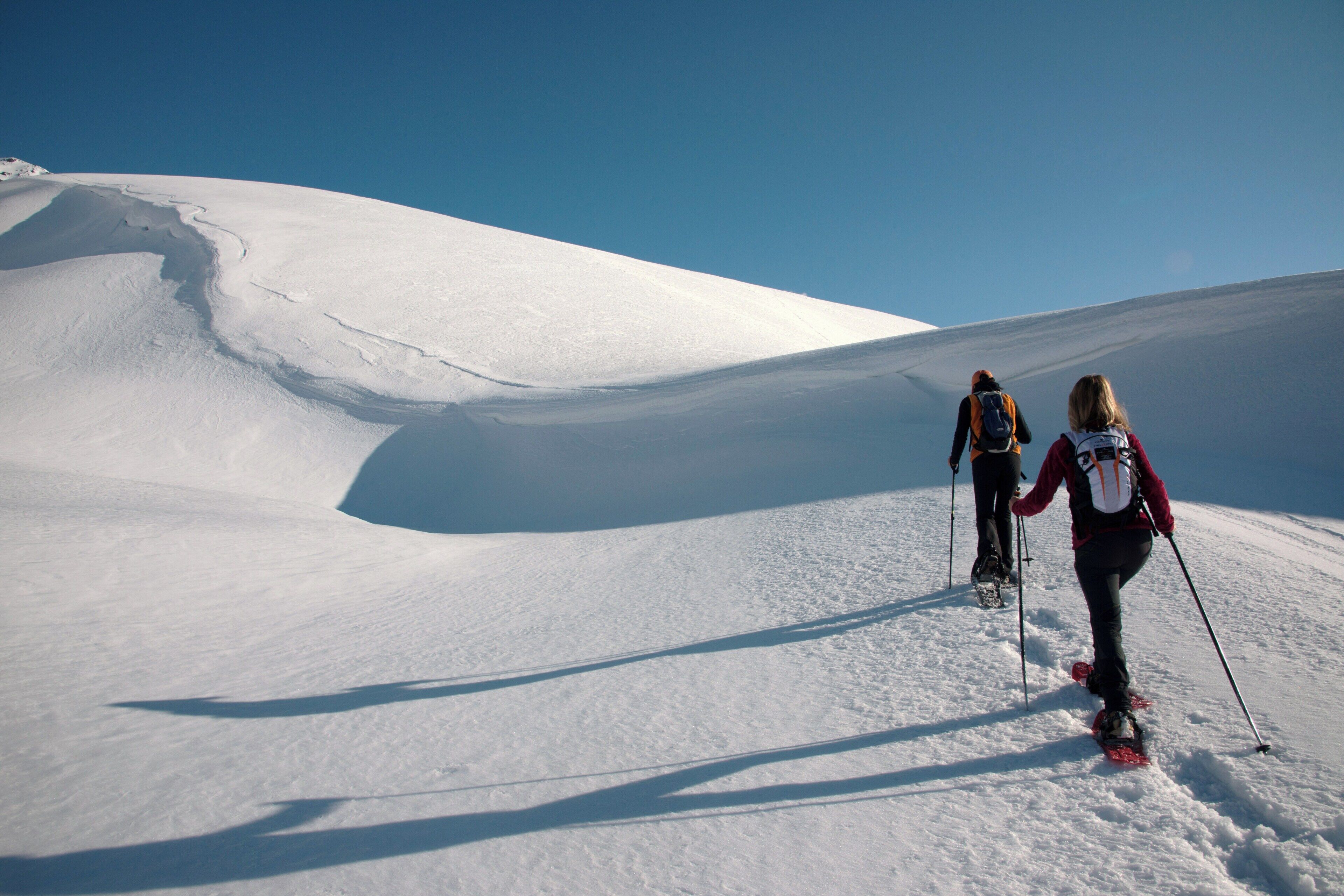 Eine verschneite Landschaft, zwei Skifahrer steigen einen Hang hinauf.