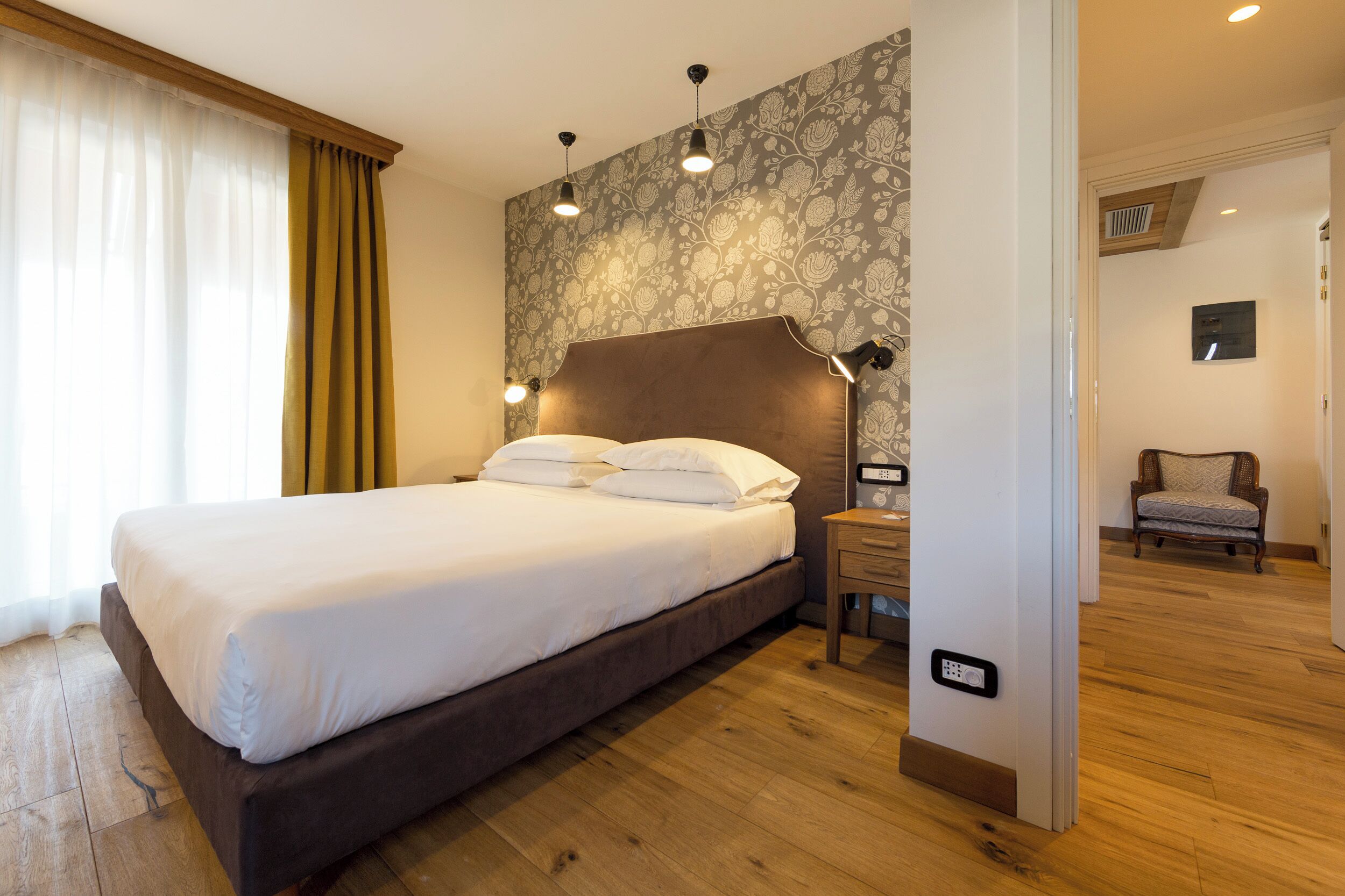 Ein Schlafzimmer mit einem großen Bett, Nachttischlampen, einem Nachttisch, einem Sessel und einer Wand mit Muster.