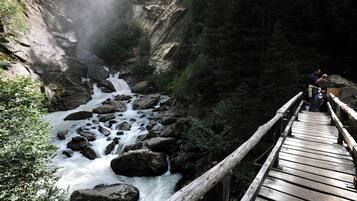Eine Holzbrücke über einem reißenden Fluss mit felsigem Ufer und dichtem Wald.