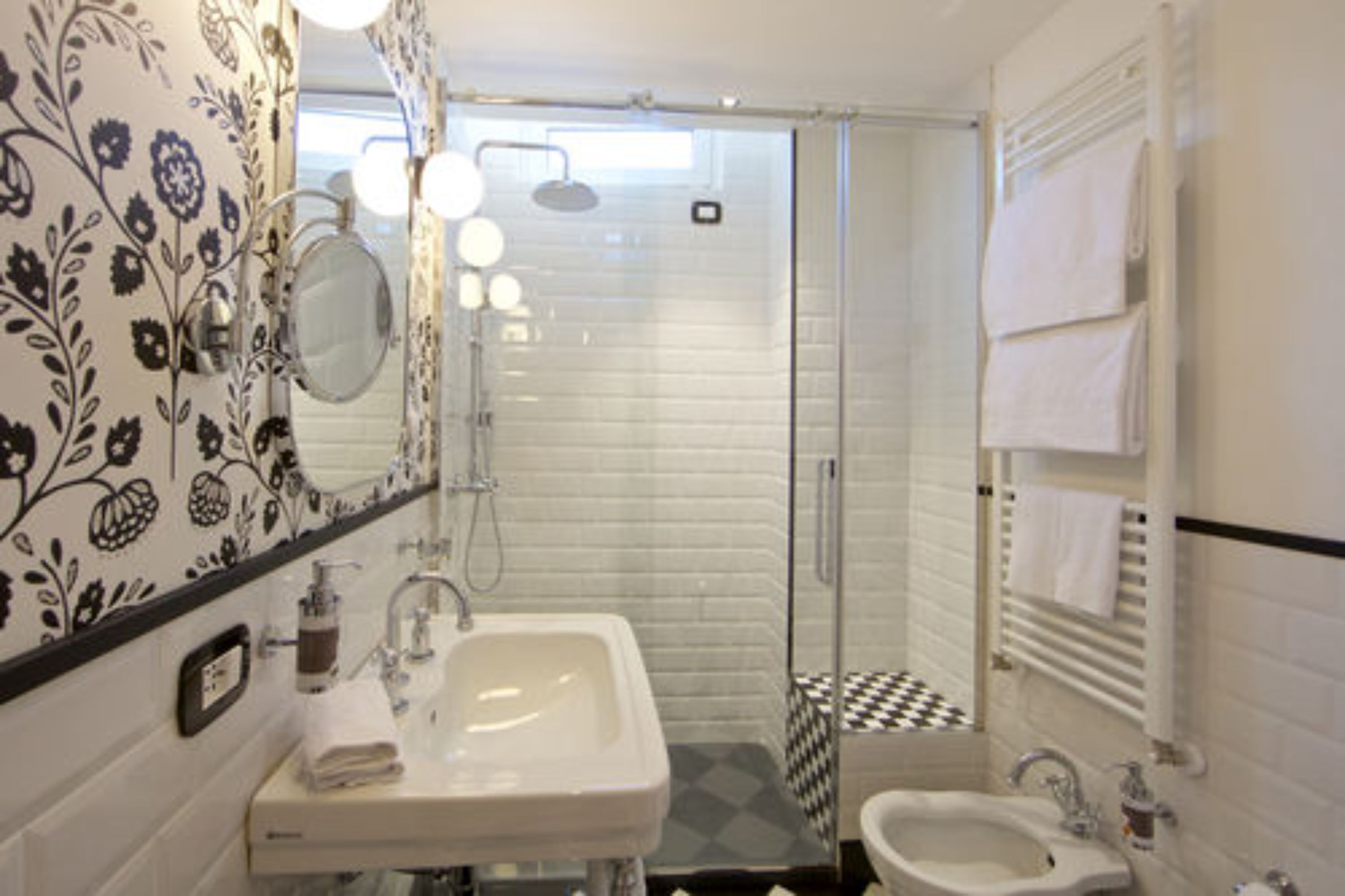 Ein Badezimmer mit einem weißen Waschbecken, einem Spiegel, einer Dusche mit Glastür und einem gefliesten Boden.