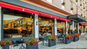 A hotel exterior with outdoor seating, large windows, and a red awning. - Hotel Duca D'Aosta (Aosta)