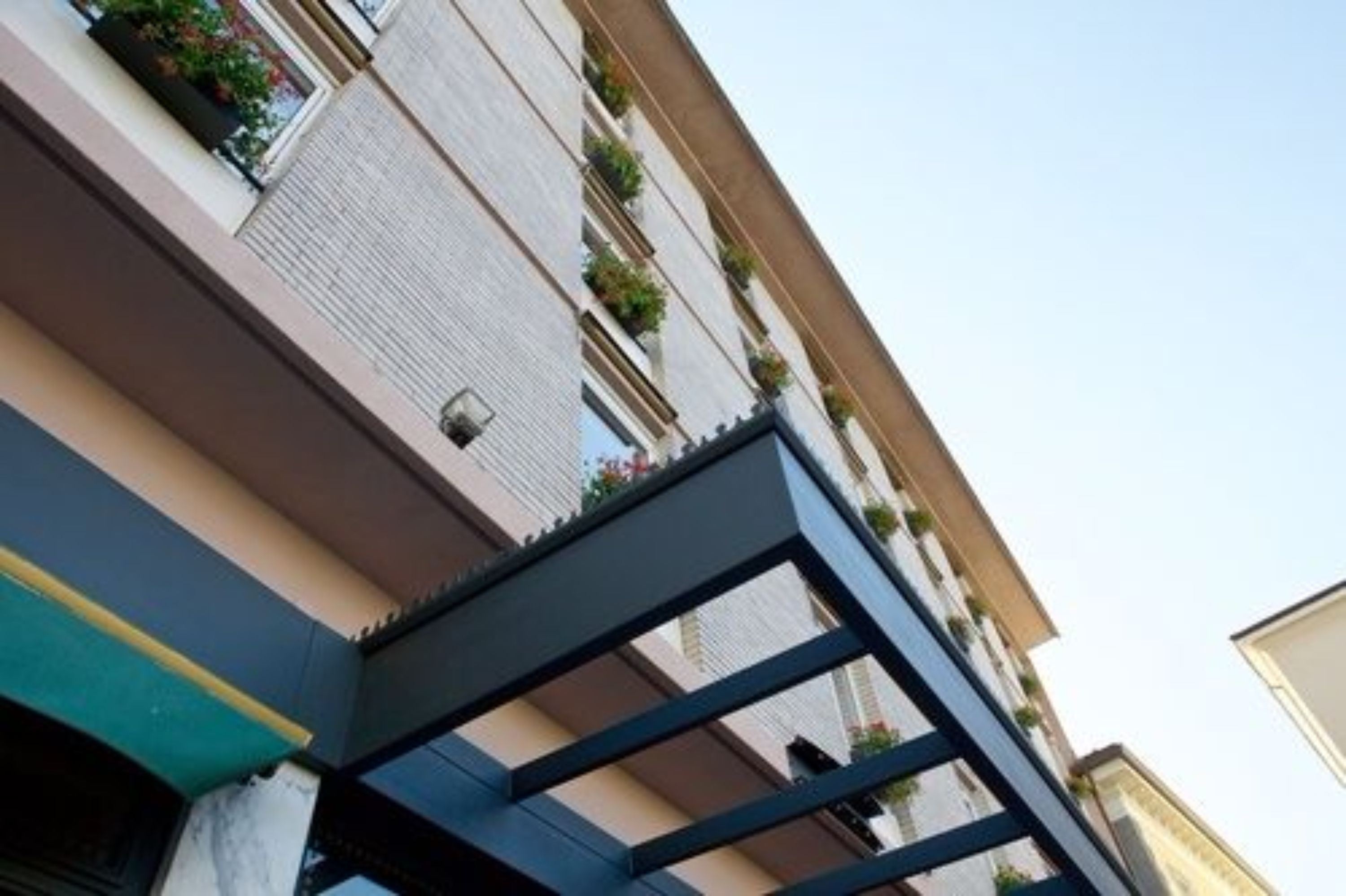 Un edificio de varios pisos con balcones, una entrada visible y un cielo despejado.