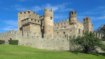 Un castillo de piedra histórico con múltiples torres y almenas, rodeado de un césped bien cuidado.