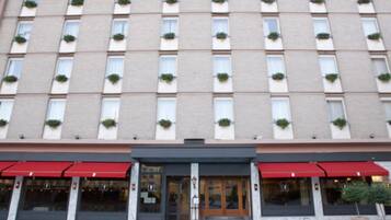 Ein mehrstöckiges Hotel mit einheitlicher Fassade, großen Fenstern mit Grünpflanzen und einer roten Markise über dem Eingang.