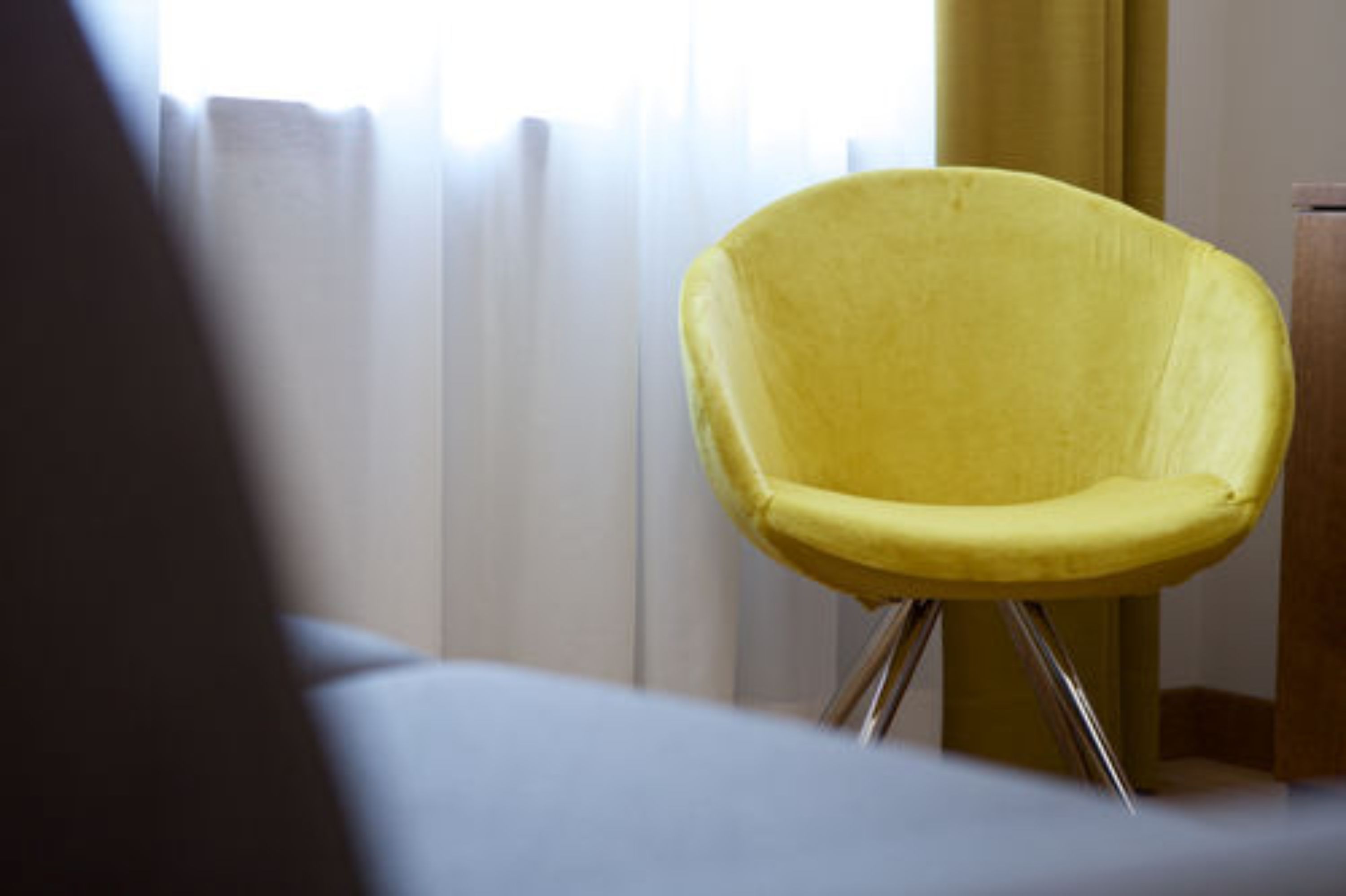 A yellow chair with a metal frame in a room with a window and curtains.