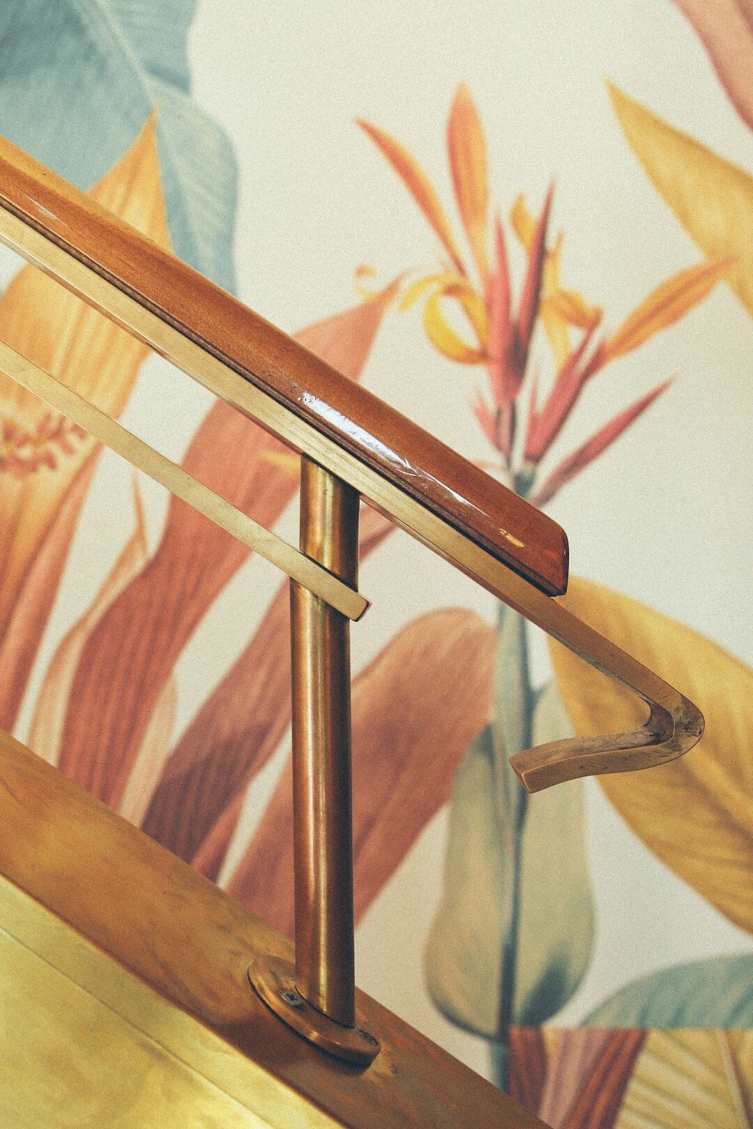 A wooden handrail with a metal bracket, set against a floral wallpaper background.