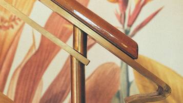 A wooden handrail with a metal bracket, set against a floral wallpaper background.