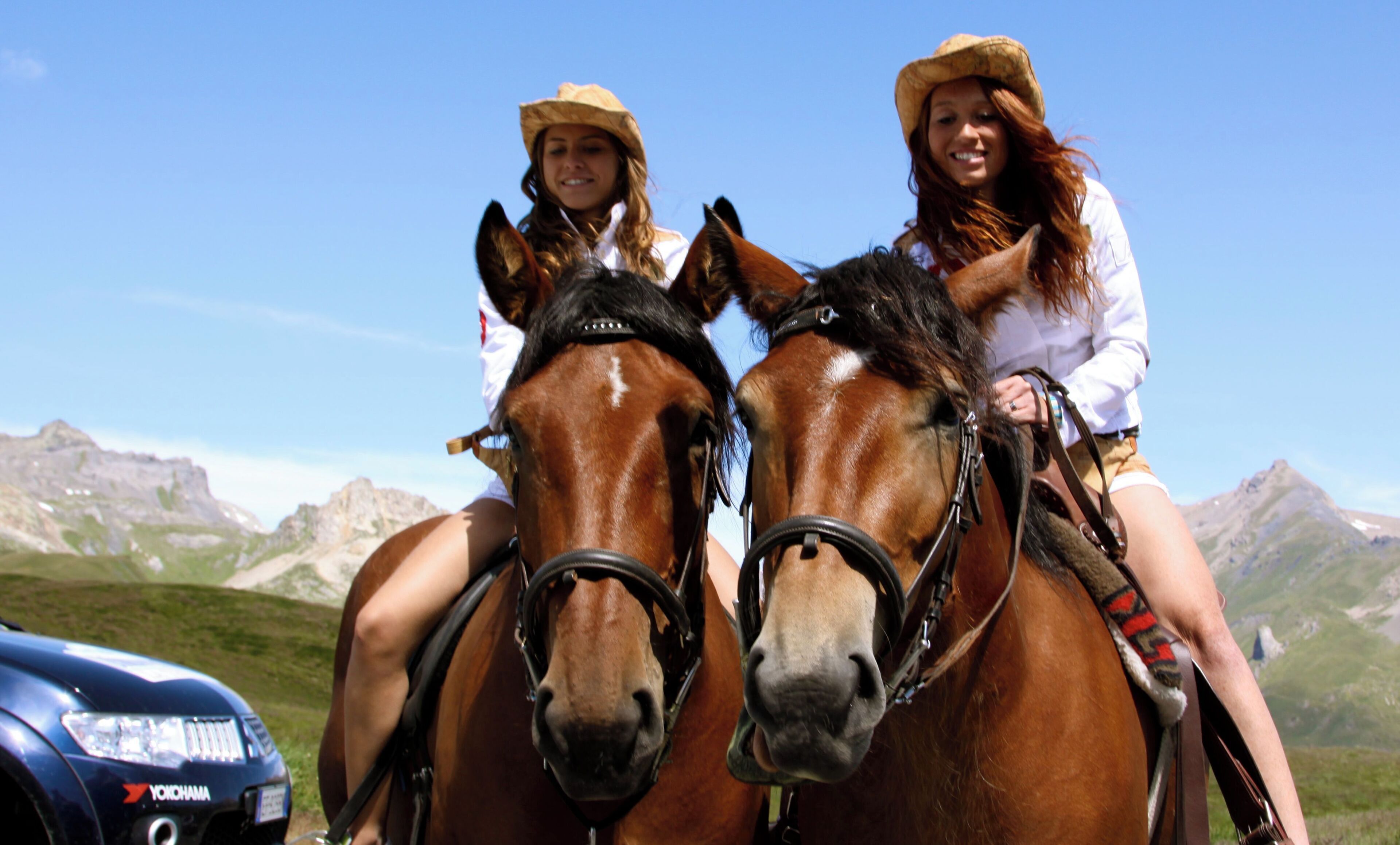 Dos personas montando a caballo con un paisaje montañoso al fondo.