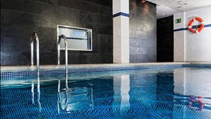 Een zwembad met helderblauw water, een metalen trap en een reddingsboei aan de muur.