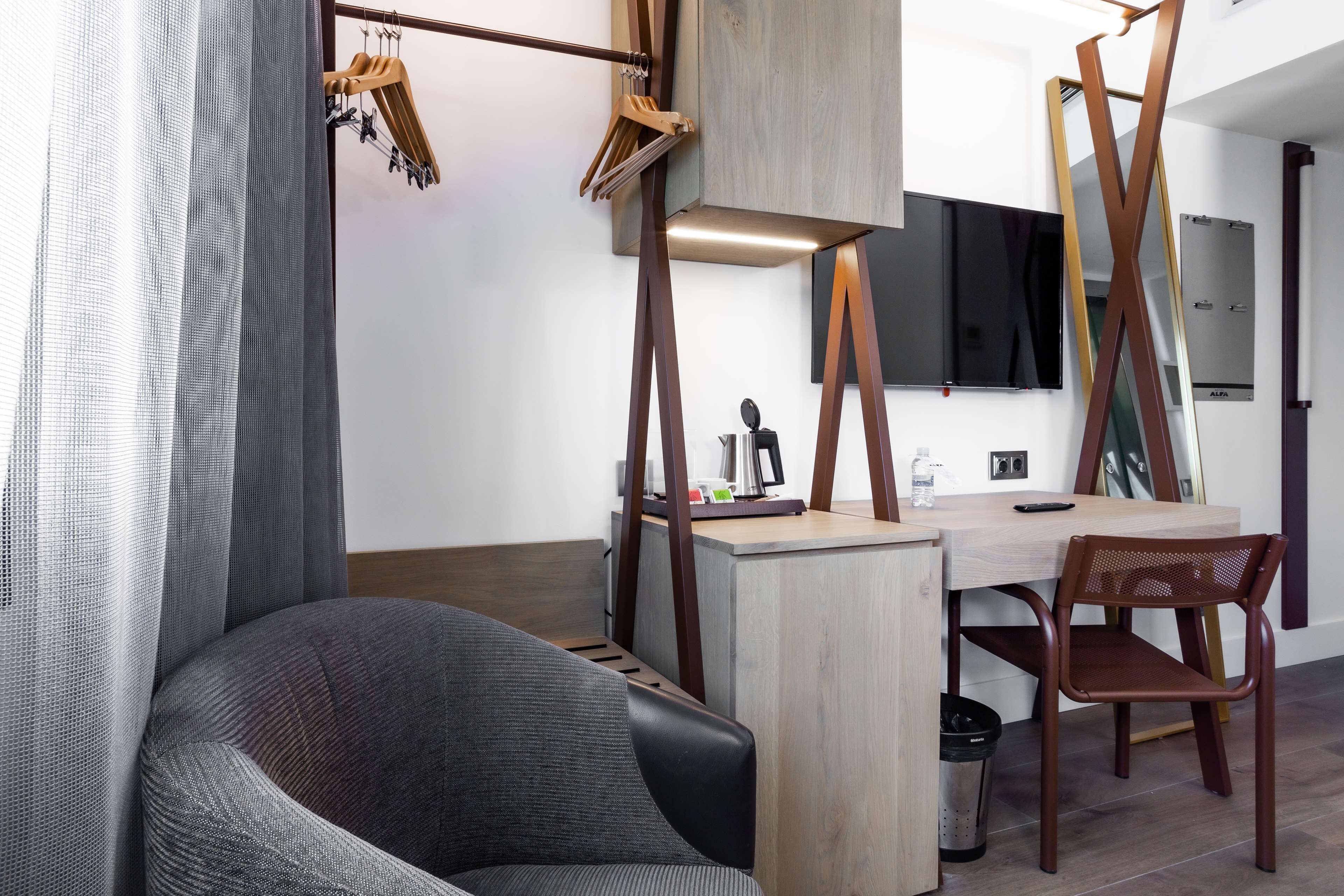 A modern room with a grey upholstered chair, a wooden desk, and a hanging clothes rack.