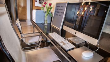 A hotel reception area with a reception desk, computer setup, and a vase with flowers.