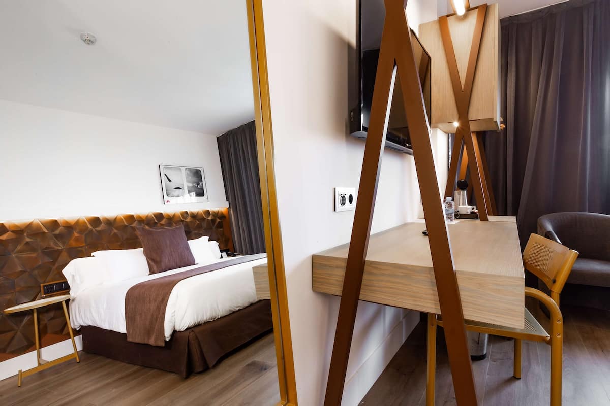 Ein Hotelzimmer mit Bett, Nachttisch, Stuhl und einem an der Wand befestigten Fernseher.