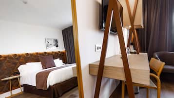 Una habitación de hotel con cama, mesita de noche, silla y televisor en la pared.
