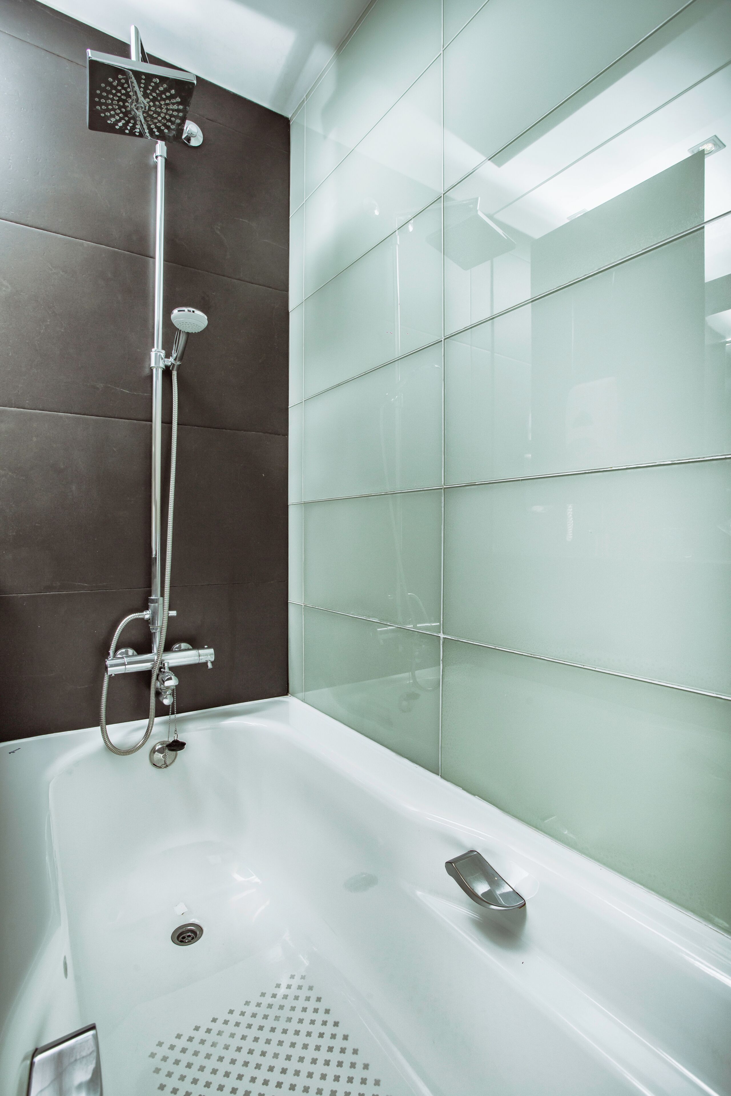 A modern bathroom with a glass shower enclosure, a white bathtub, and a dark tiled wall.