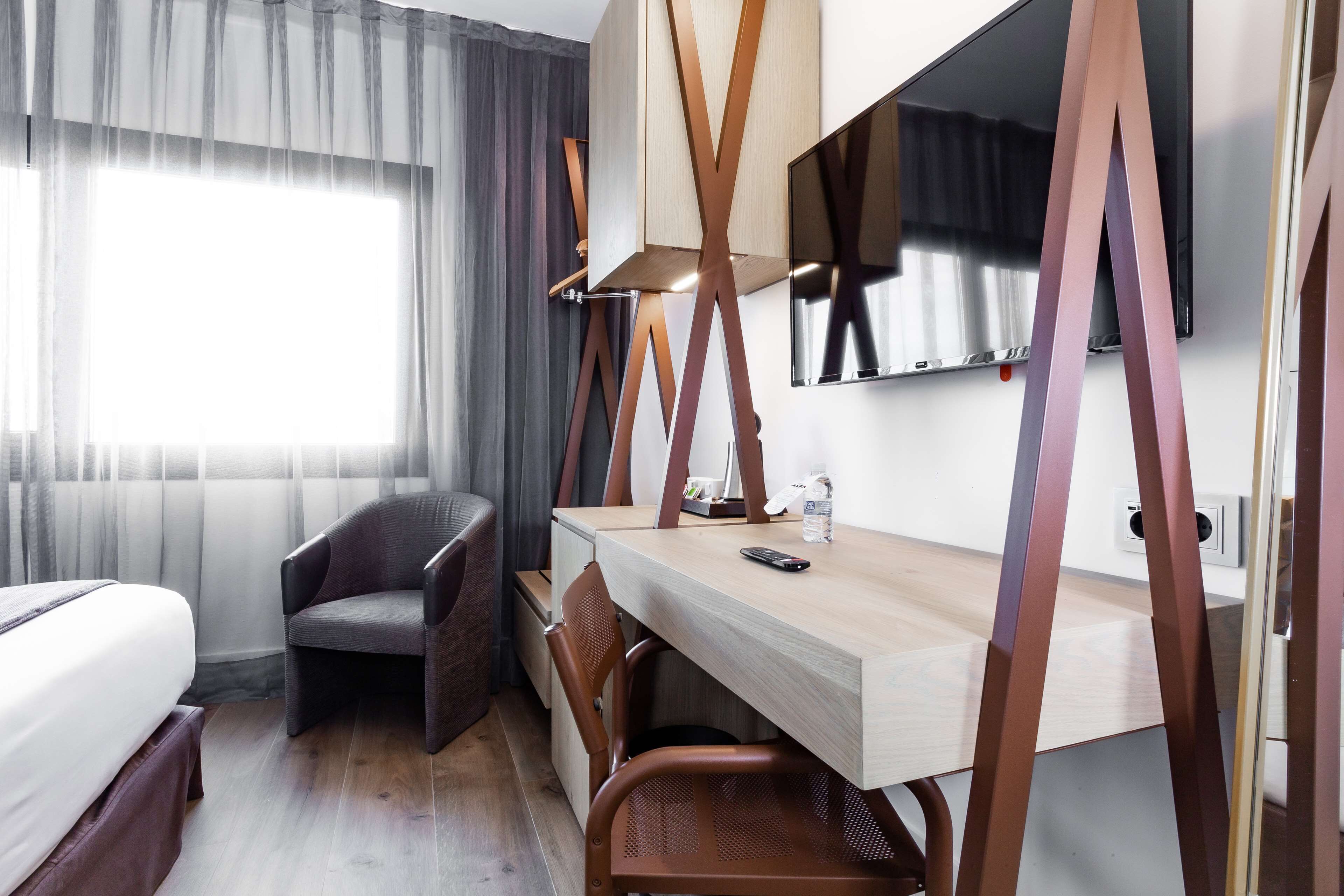 Habitación de hotel con cama, escritorio, silla, televisor y ventana con cortinas.