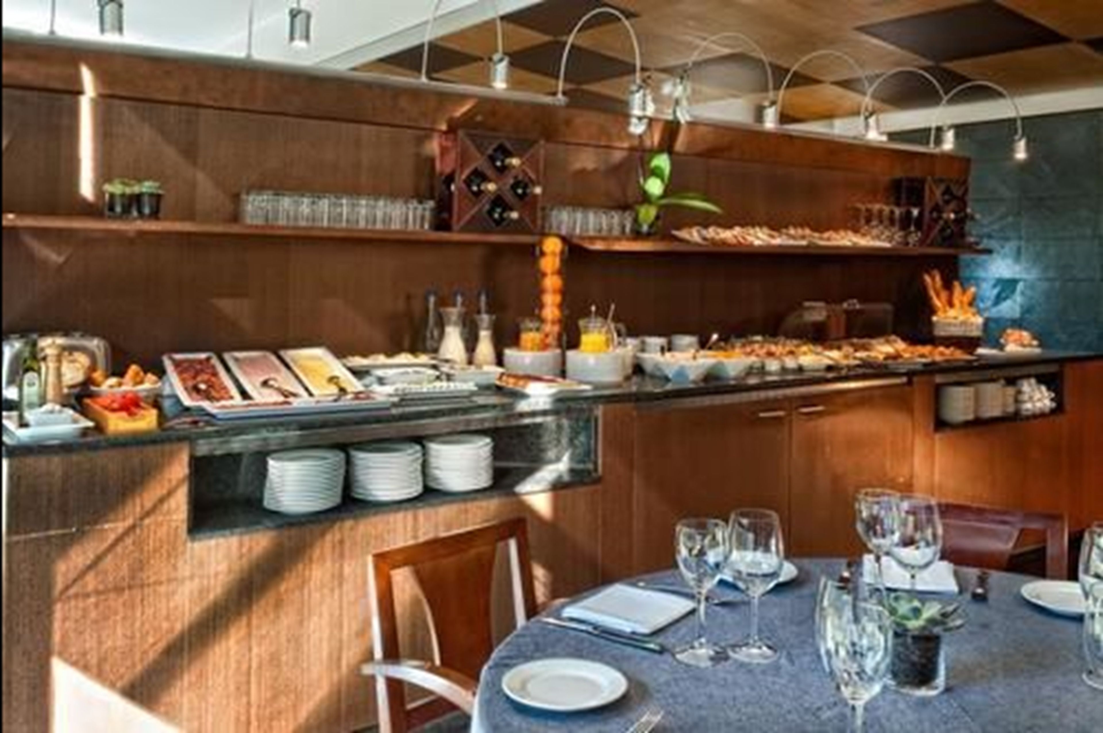 Een buffetopstelling met diverse gerechten en drankjes, een bar met glazen en een eettafel gedekt met borden en glazen.