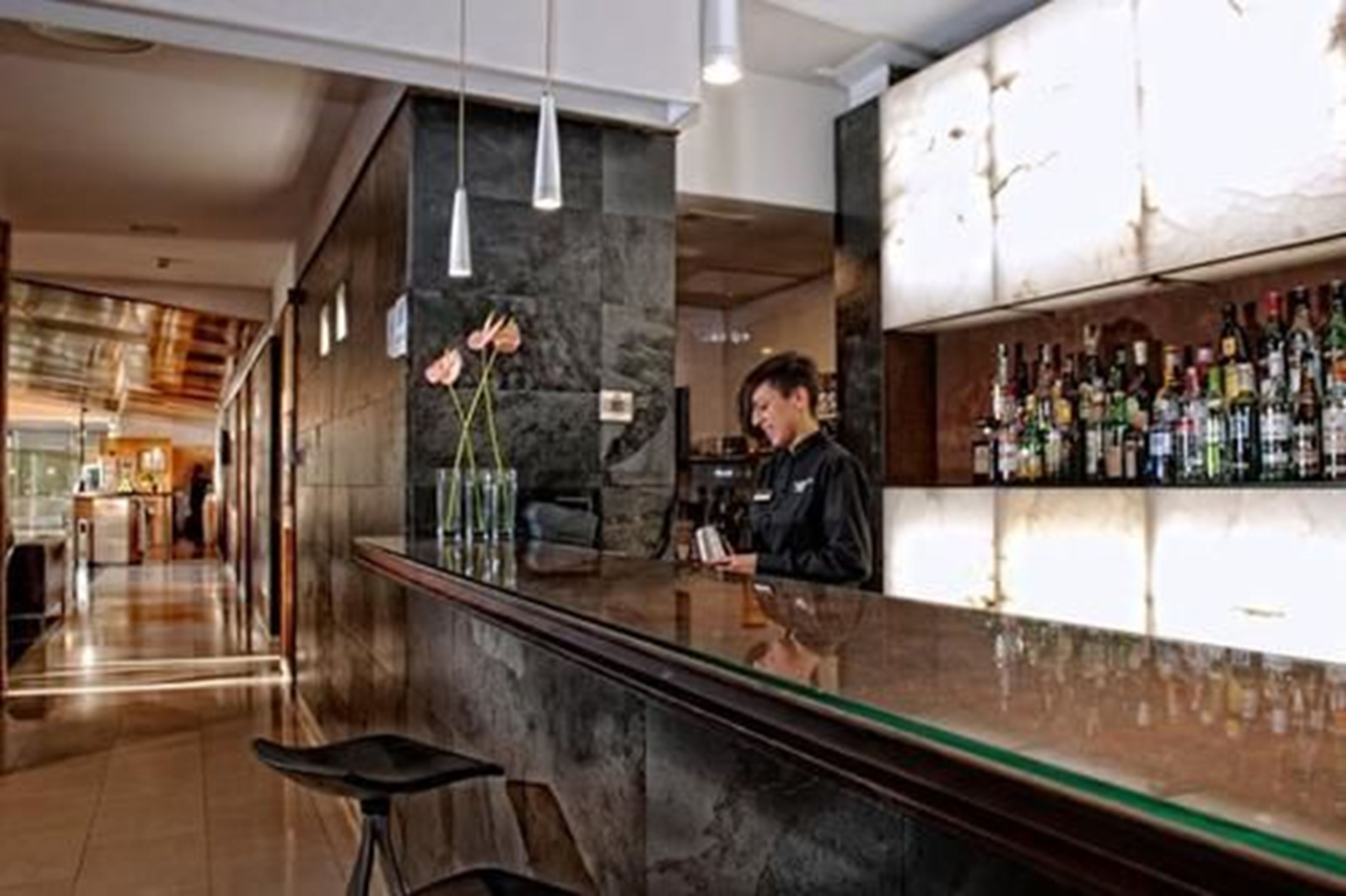 Un espace bar moderne doté d’un comptoir en marbre, de luminaires suspendus et d’un barman.