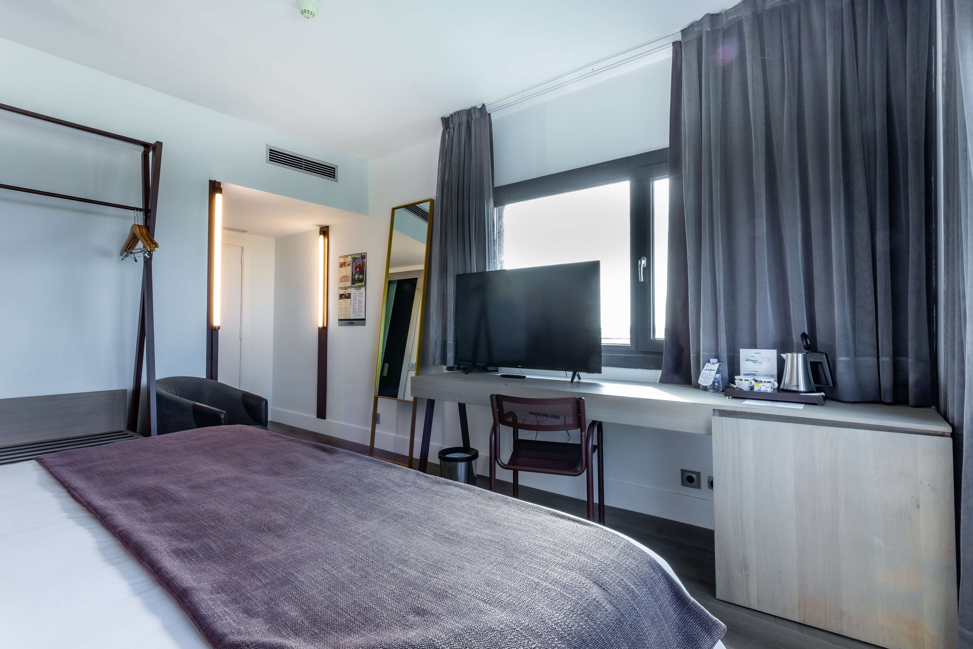 A hotel room with a bed, a desk with a TV, a chair, and a small cabinet.