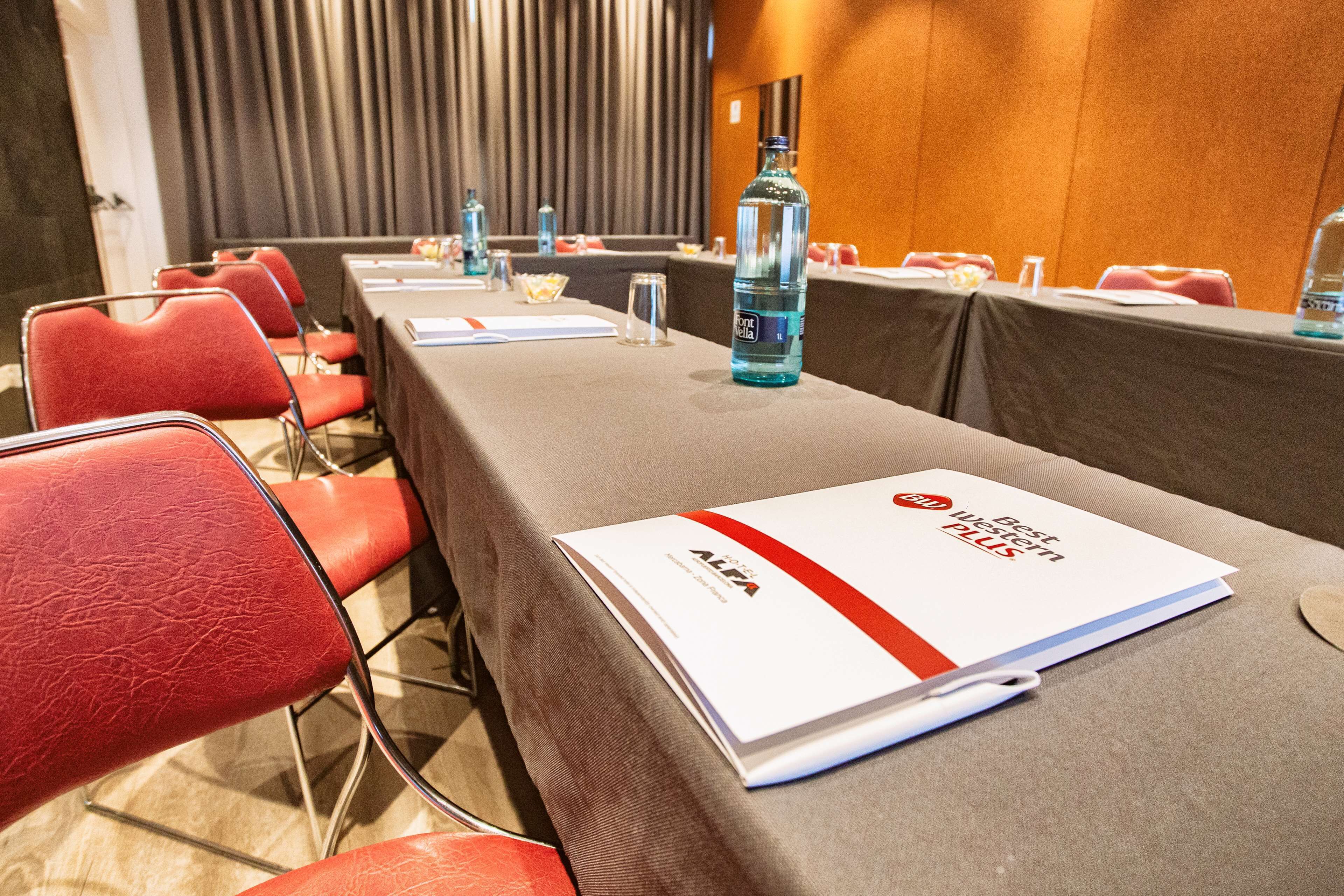 Une salle de conférence avec des chaises rouges, une table sur laquelle est posée une brochure et une bouteille d’eau.