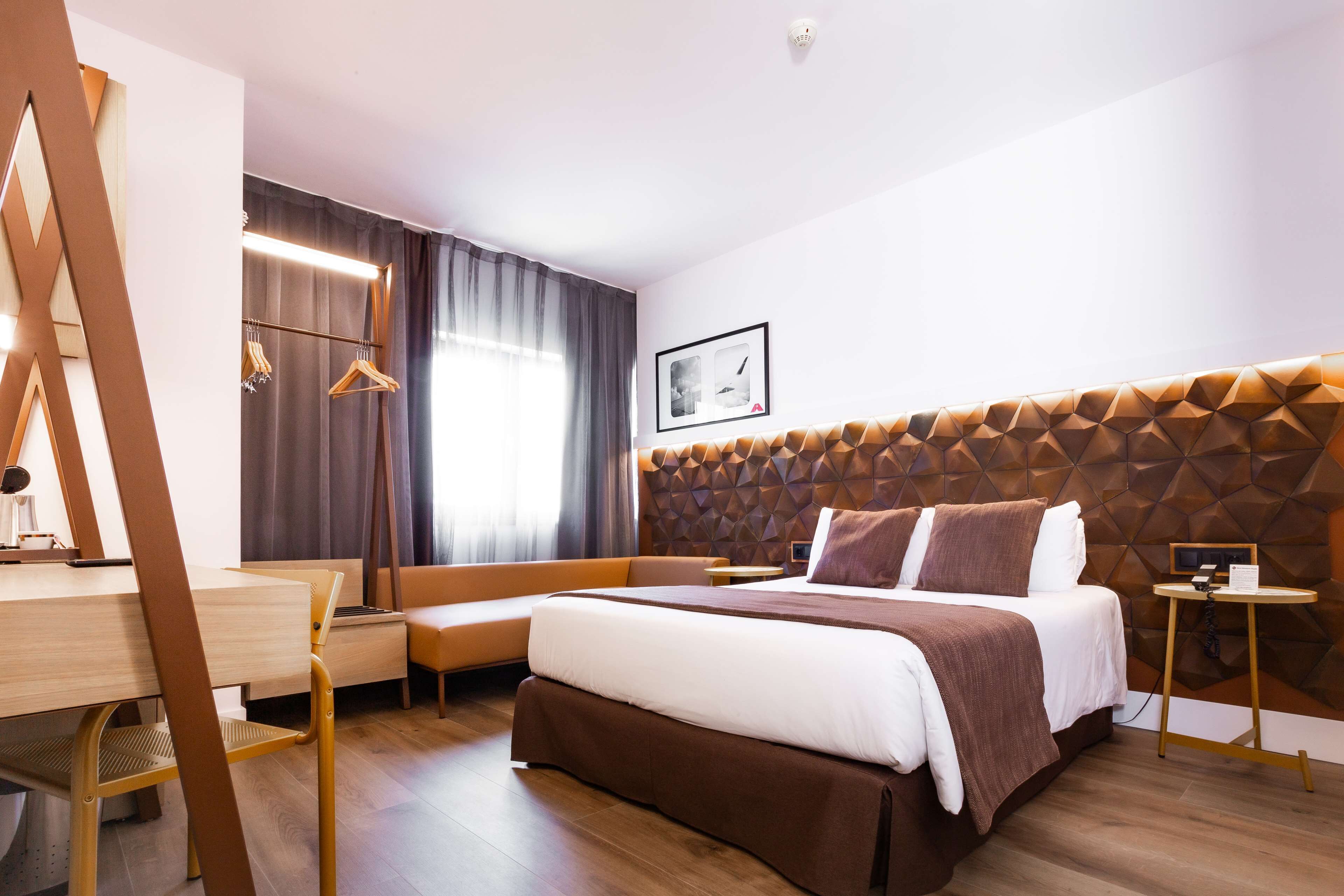 A modern hotel room with a large bed, a desk, and a seating area.