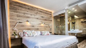 Een moderne slaapkamer met een houten hoofdbord, een groot bed met witte lakens, twee bedlampjes en een nachtkastje met een kleine plant.