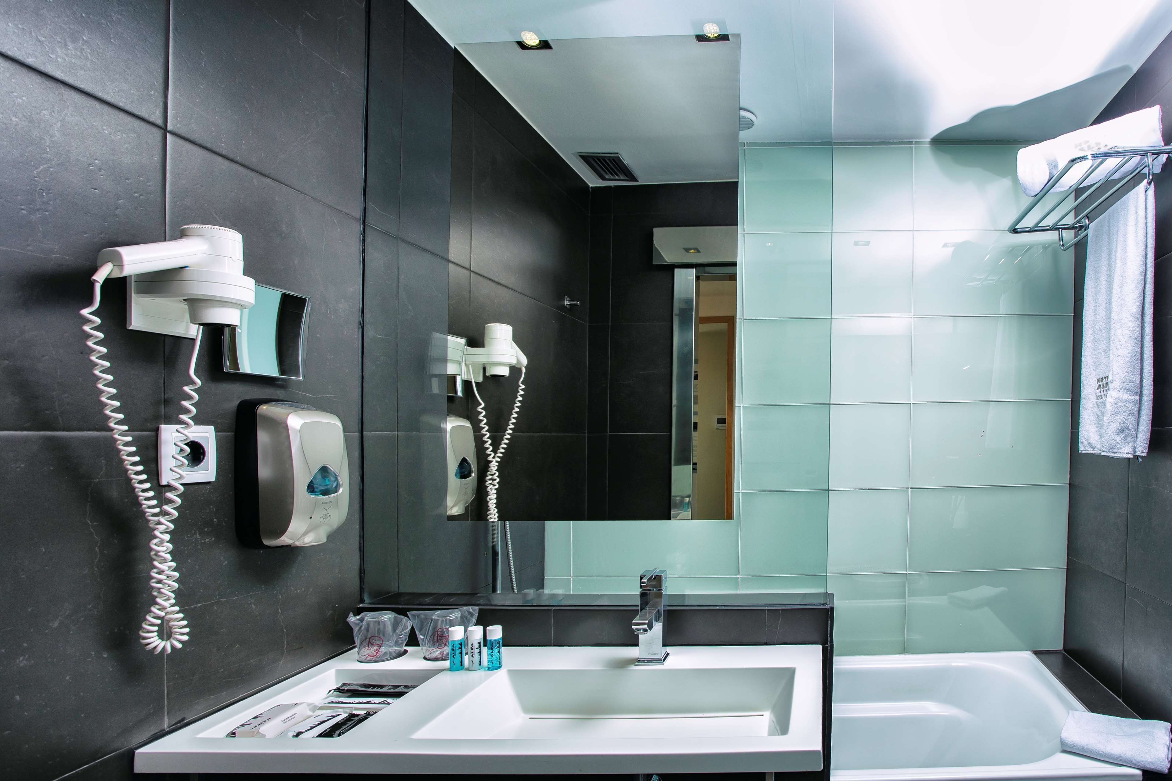 A modern bathroom with a white sink, a mirror, a hairdryer, and a towel rack.