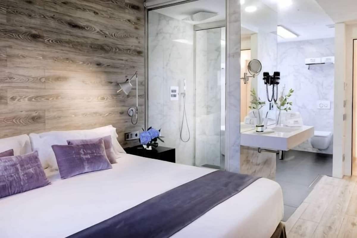 Ein modernes Schlafzimmer mit einem Holzkopfteil, einem großen Bett, einem Nachttisch mit Lampe und einer Duschkabine aus Glas.